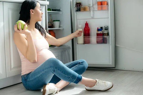 Mujer Embarazada Sosteniendo Manzana Mientras Está Sentada Suelo Mirando Nevera — Foto de Stock