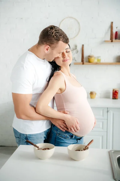 Smiling Pregnant Couple Hugging Kitchen Cereals Bowls — Stock Photo, Image