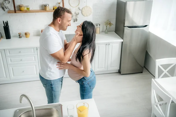 美丽快乐的怀孕夫妇在厨房里拥抱橙汁 — 图库照片