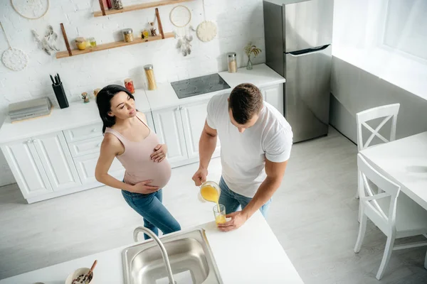 快乐的怀孕妻子在厨房里 丈夫倒橙汁 — 图库照片