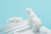 Toy polar bears on coffee lids on blue background, animal welfare concept