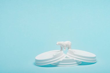 Toy polar bear on plastic coffee lids on blue background, animal welfare concept clipart