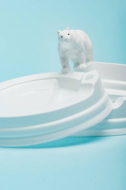 Mavi arka planda plastik kahve kapakları üzerinde oyuncak kutup ayısı, hayvan refahı konsepti