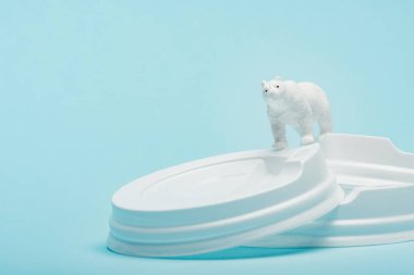 Mavi arka planda plastik kahve kapakları üzerine oyuncak kutup ayısı, ekolojik problem kavramı