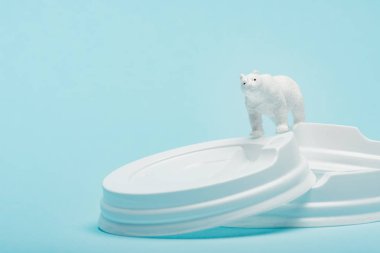 Toy polar bear on plastic coffee lids on blue background, ecological problem concept clipart