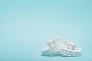 Mavi arka planda plastik kahve kapağı olan iki oyuncak kutup ayısı, ekolojik problem kavramı