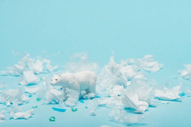 Mavi arka planda plastik çöpleri olan beyaz oyuncak kutup ayısı, hayvan refahı konsepti
