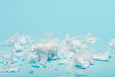 White toy polar bear with plastic garbage on blue background, animal welfare concept clipart