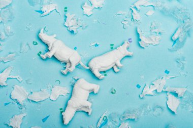 Top view of hippopotamus, rhinoceros and bear toys with plastic garbage on blue background, animal welfare concept