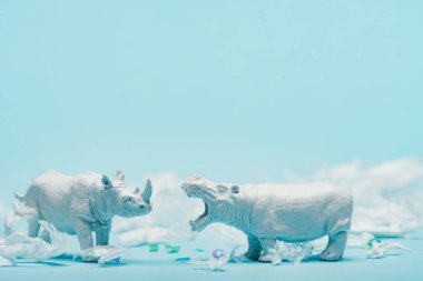 Beyaz su aygırları ve gergedan oyuncakları mavi arka planda plastik çöp, hayvan refahı konsepti