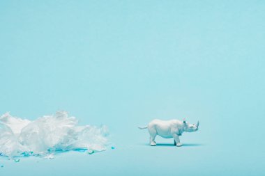 White rhinoceros toy and plastic garbage on blue background, animal welfare concept clipart