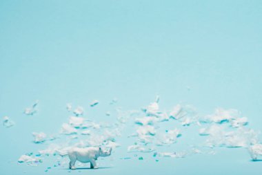 White rhinoceros toy and plastic garbage on blue background, environmental pollution concept clipart