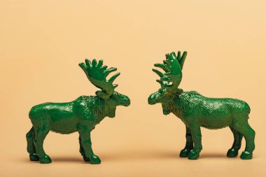 Green toy mooses on yellow background, hunting for horns concept clipart