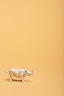White toy rhinoceros on yellow background, animal welfare concept clipart