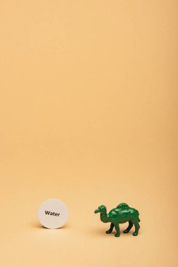 Green toy camel with lettering water on card on yellow background, water scarcity concept clipart