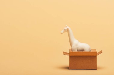 White toy giraffe in cardboard box on yellow background, animal welfare concept clipart