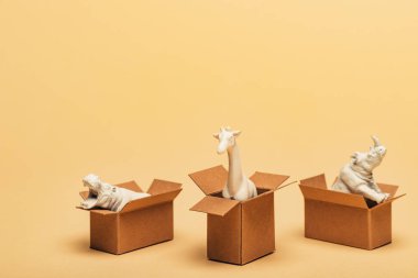White toy hippopotamus, rhinoceros and giraffe in cardboard boxes on yellow background, animal welfare concept clipart