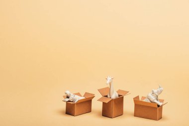 White toy hippopotamus, rhinoceros and giraffe in cardboard boxes on yellow background, animal welfare concept clipart
