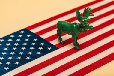 Green toy moose on american flag on yellow background, animal welfare concept clipart