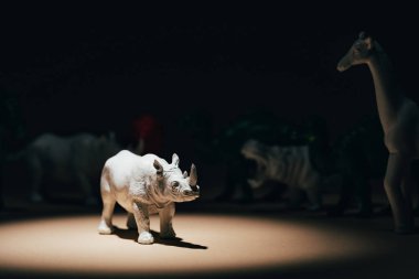 White toy rhinoceros under spotlight with animals at background, voting concept clipart