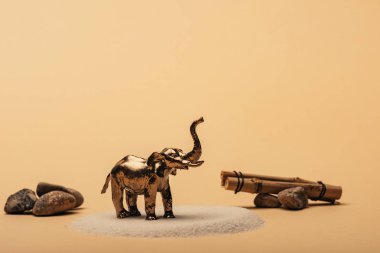Toy elephant on sand with stones and wooden sticks on yellow background, animal welfare concept clipart