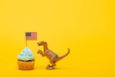Oyuncak dinozor kek yanında sarı arka planda Amerikan bayrağı