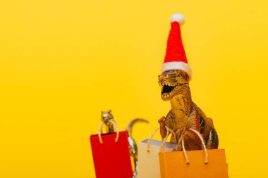 Noel Baba şapkalı ve sarı arka planda alışveriş torbalı oyuncak dinozorların seçici odağı