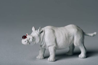 White toy rhinoceros with blood on grey background, hunting for horn concept clipart