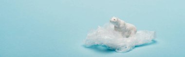 Oyuncak kutup ayısının mavi arka planda plastik paketi üzerindeki panoramik çekimi, çevre kirliliği konsepti