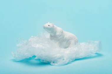 Toy polar bear on plastic packet on blue background, environmental pollution concept clipart