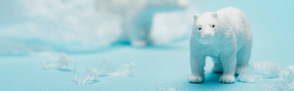 Panoramic shot of toy polar bears with polyethylene trash on blue background, environmental pollution concept