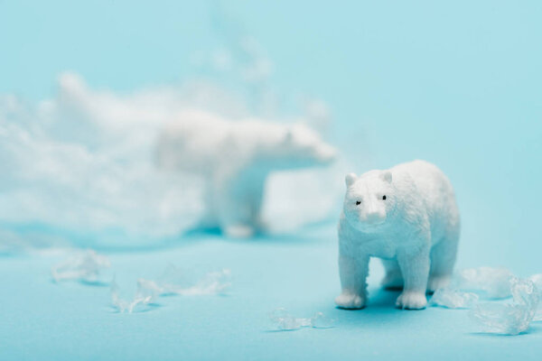 Toy polar bears with polyethylene trash on blue background, environmental pollution concept