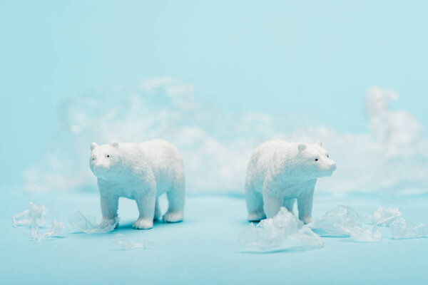 Toy polar bears with polyethylene trash on blue background, animal welfare concept