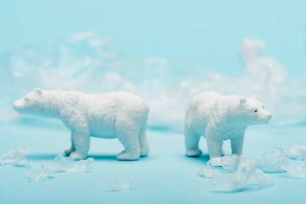 Two toy polar bears with polyethylene trash on blue background, animal welfare concept