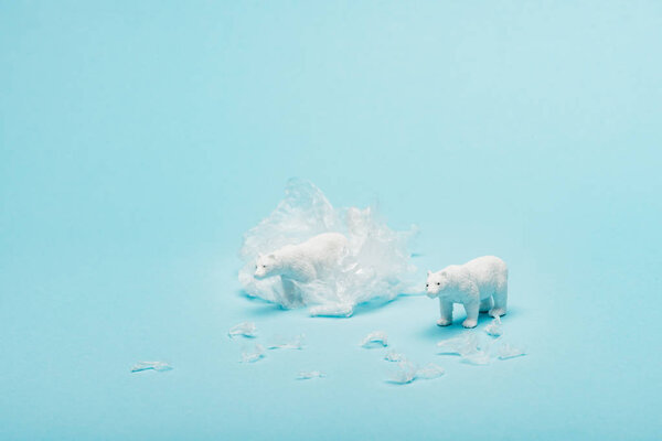 Toy polar bears with polyethylene trash on blue background, animal welfare concept