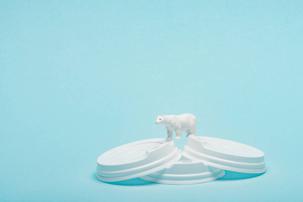Toy polar bear on plastic coffee lids on blue background, animal welfare concept