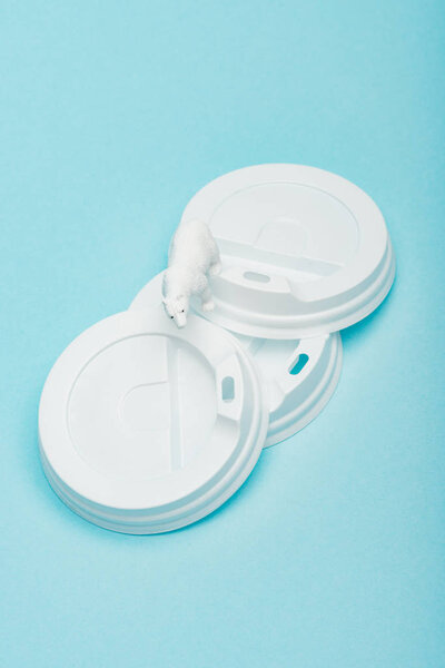 Top view of toy polar bear on plastic coffee lids on blue background, animal welfare concept