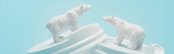 Panoramic shot of toy polar bears on plastic coffee lids on blue background, animal welfare concept