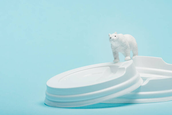 Toy polar bear on plastic coffee lids on blue background, ecological problem concept