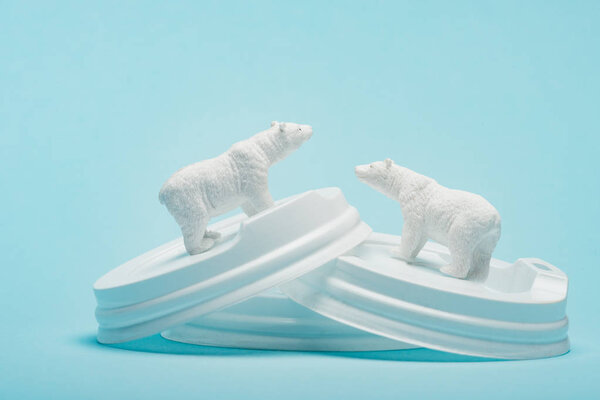 Toy polar bears on plastic coffee lids on blue background, ecological problem concept