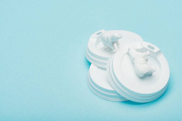Toy polar bears on plastic coffee lids on blue background, animal welfare concept