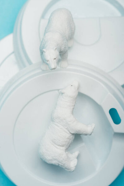 Top view of toy polar bears on plastic coffee lids on blue background, animal welfare concept