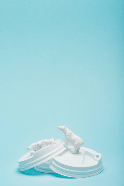 Toy polar bears on coffee lids on blue background, animal welfare concept