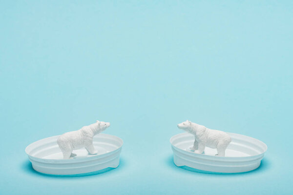 Two toy polar bears on coffee lids on blue background, animal welfare concept