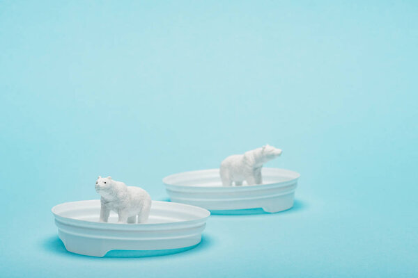 Toy polar bears on plastic coffee lids on blue background with copy space, animal welfare concept