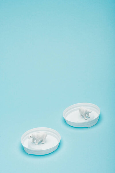 White toy polar bears on plastic coffee lids on blue background, animal welfare concept