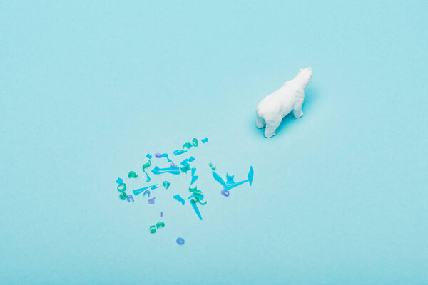 High angle view of of toy polar bear and plastic pieces on blue background, animal welfare concept