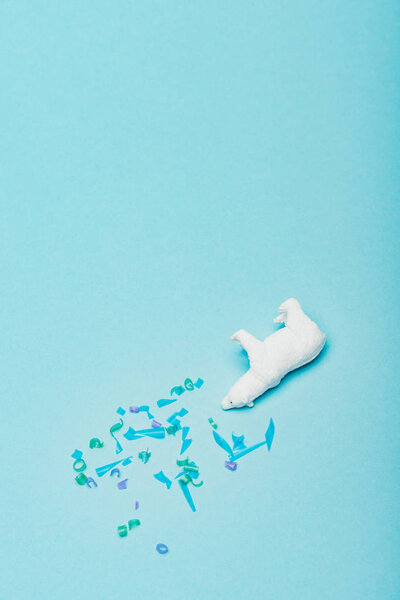 Top view of of toy polar bear with plastic pieces on blue background, animal welfare concept