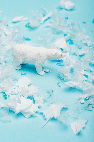 Toy polar bear with polyethylene and plastic pieces on blue background, animal welfare concept