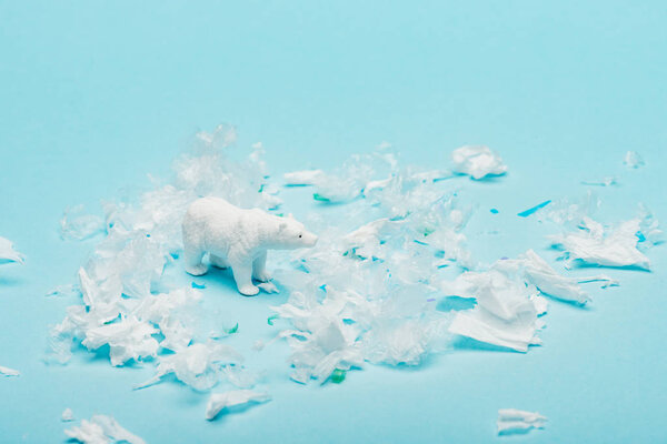 Toy polar bear with polyethylene and plastic garbage on blue background, animal welfare concept